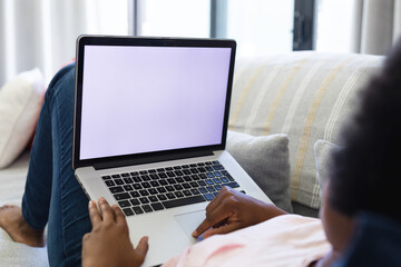 African american girl using laptop while lying on sofa in living room at home, copy space