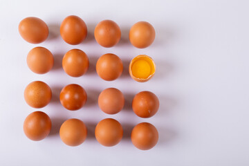 Overhead view of brown eggs with one broken egg arranged in square on table with blank space