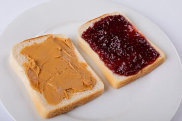 Close-up of open face peanut butter and jelly sandwich in plate on white background