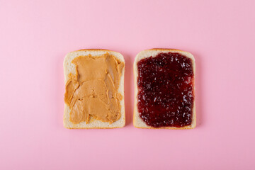 Directly above shot of peanut butter and preserves on bread slices over pink background