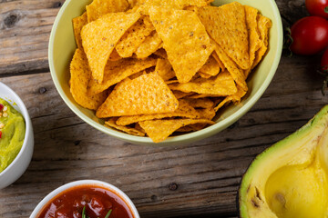 Close-up of nacho chips in bowl with dips and vegetables on table