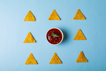 Overhead view of red sauce with rosemary amidst nacho chips arranged on blue background © wavebreak3