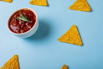Foto op Plexiglas High angle view of red sauce with rosemary by nacho chips over blue background © WavebreakMediaMicro