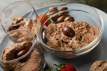 Chocolate mousse with coated nuts and strawberries served in bowl and glasses on plate