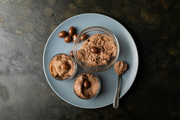 Overhead view of chocolate mousse with coated nuts served in bowl and glasses on plate at table