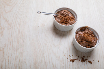Chocolate mousse with cocoa powder and spoons served in ramekin bowls on table with blank space