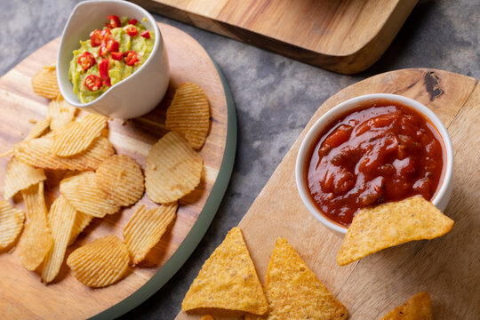 High angle view of potato chips and nacho chips with various salsa on serving board at table