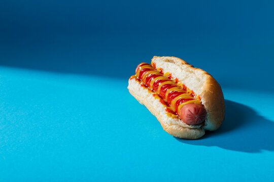 Close-up of hot dog with tomato and mustered sauce over blue background with copy space