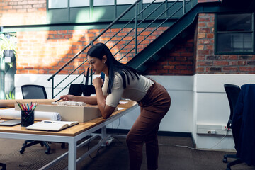 Side view of biracial young female architect analyzing building model at desk in modern office