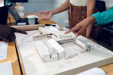 Multiracial young male and female architects pointing over building model during discussion
