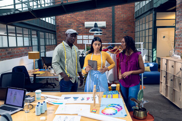 Multiracial young male and female fashion designers discussing design over digital tablet at desk