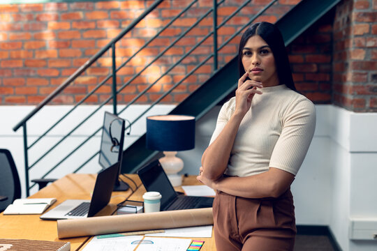 Portrait of confident biracial young businesswoman standing by blueprints at desk in modern office