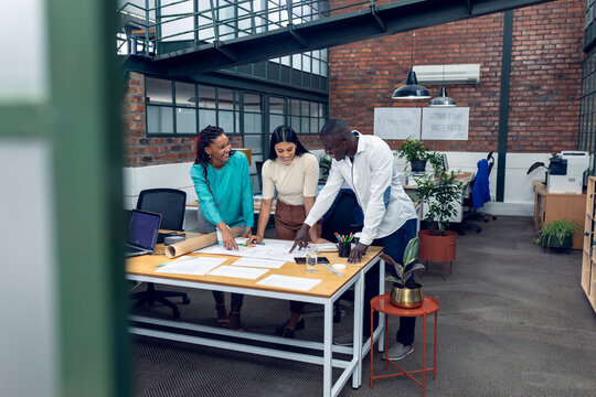 Happy multiracial young male and female architects planning while gesturing over blueprint at desk