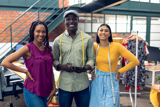 Portrait of smiling multiracial male and female fashion designers standing with digital tablet