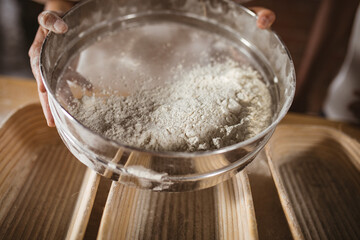 Cropped hands of asian mid adult female baker showing strainer with flour
