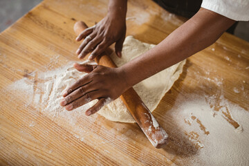 High angle view of cropped hands of african american mid adult male baker rolling dough at table