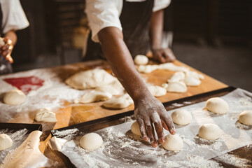 Midsection of african american mid adult male baker picking dough ball while making bread in bakery