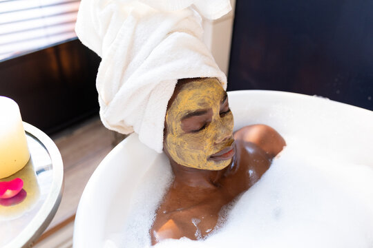 High angle view of african american woman with face mask relaxing in bath tub at home