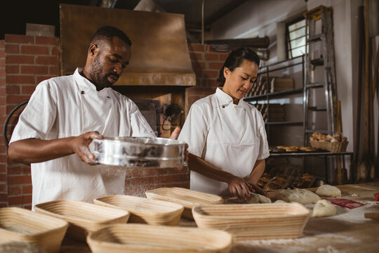 African american mid adult male baker with mid adult asian female coworker working in bakery