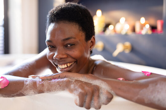 Portrait of smiling african american young woman enjoying bathing in bath tub at home