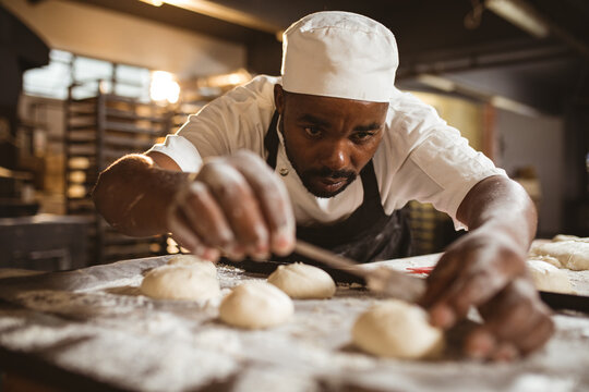 African american mid adult male baker making cross with blade on dough while working in bakery