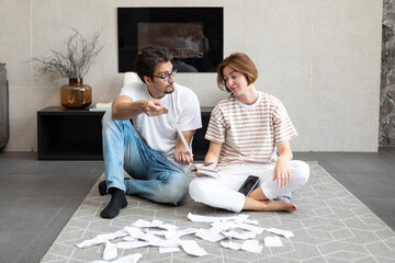 Shocked and depressed married couple sitting on the floor and demonstrating many bills, stressed and confused by calculate expense from invoice or bills, have no money to pay mortgage or loan