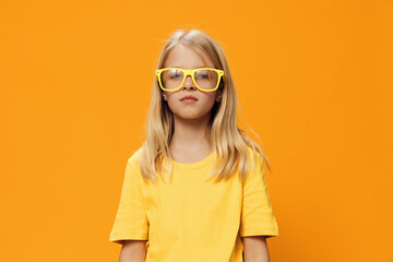 portrait of a cute beautiful school-age girl in yellow glasses for vision on a yellow background, pleasantly smiling looking at the camera