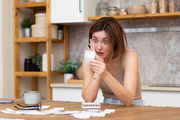 Close up of shocked woman sitting at the table, stressed and confused by calculate expense from invoice or bills, have no money to pay mortgage or loan. High prices and spending money concept