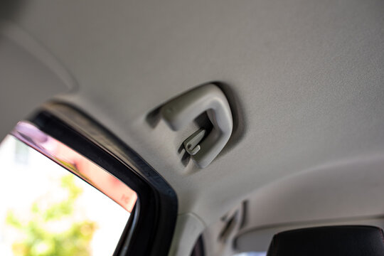 White hand grip from the back seat on the white ceiling of a Japanese car.