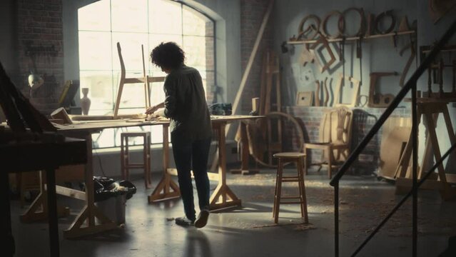 Multiethnic Artisan Woodworker Entering Loft Studio, Starting to Work on a Wooden Chair with an Electric Drill. Black Female Carpenter Working in Workshop with Tools on the Walls.