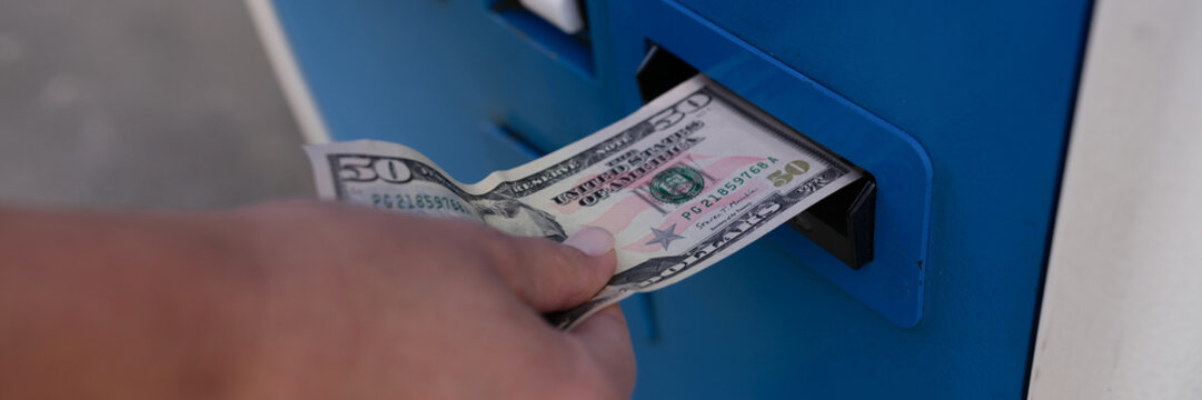 Woman inserting dollar bills into ATM on street closeup