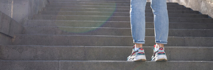 Fototapeta na wymiar Tired woman in sneakers standing in front of long staircase with steps