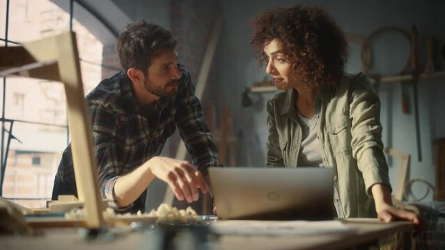 Portrait of Happy Young Business Couple Using Laptop Computer in Designer Furniture Studio. Carpenter and Designer Have Fun, DIscussing and Talking About Upcoming Orders of Wooden Furniture.
