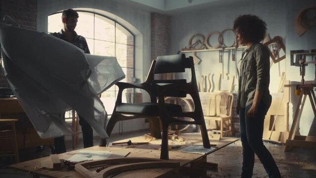 Furniture Designer Presenting His New Armchair to a Female Colleague or Client. Carpenter Removing the Cover from a Stylish Modern Lounge Chair. Small Business Owners High Five Each Other.