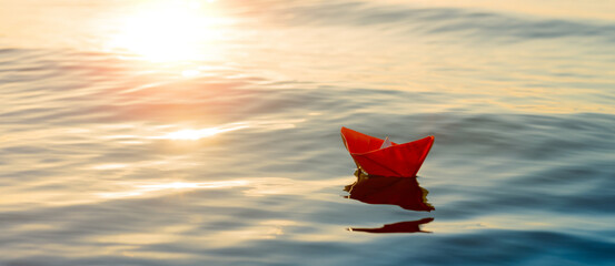 paper boat sails into the sea, a small origami ship on the water in the setting sun, travel concept. Taking trip - obrazy, fototapety, plakaty