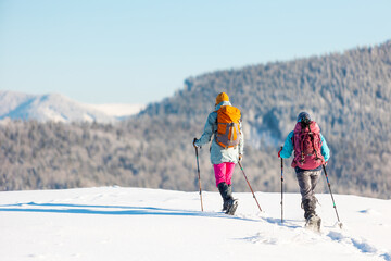 two girls in snowshoes walk in the snow. hiking in the mountains in winter.