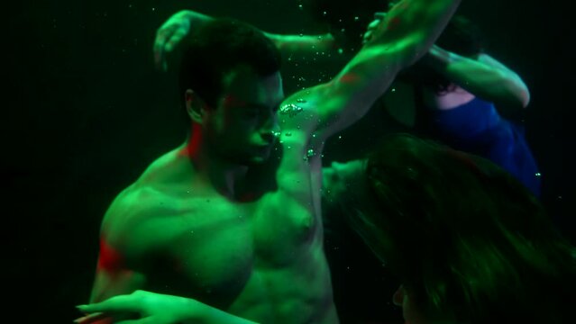 close-up of a man with a naked torso and two women in dark water. green and red light