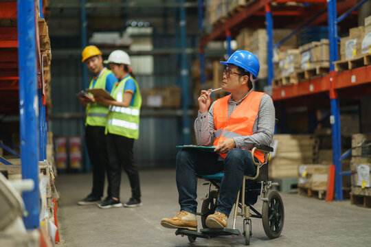 Manager handicapped in wheelchair man employee using tablet check stock work at warehouse. Worker wearing high visibility clothing and hard hat, helmet and checking count up goods boxes for delivery.