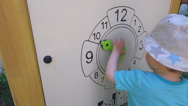 A child plays with a wooden clock on the playground. Copy space - the concept of the development of children's mathematics, learning center, counting skills, elementary school, educational games