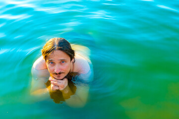  caucasian man floating in a swimming lake with blue water