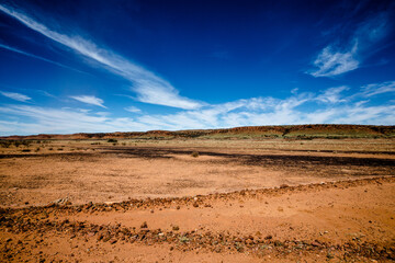 The centre of the Australian destert on Aboriginal land with bright blue sky, red earth and clouds. 