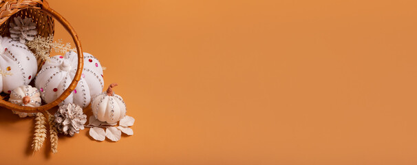 Banner with white decorative hand made pumpkins with shiny stones and pine cones in basket on colored background. Autumn harvest concept