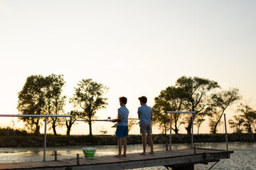 children with fishing rods stand on a wooden pier and fish at the lake. Fishing