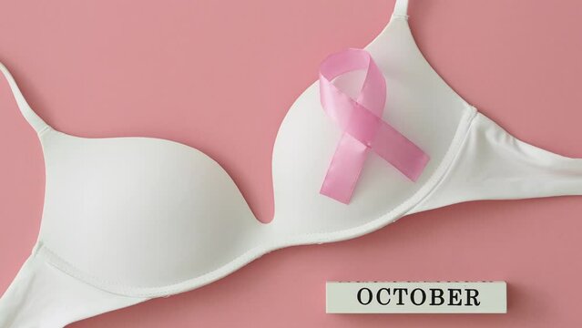 Women's white bra on a pink background with a pink bow - a symbol of breast cancer. Top view removal camera. Health care, International Women's Day and World Cancer Day concept