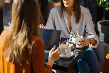Two young business women in a cafe having one on one meeting. Friends after work talking gossiping and having coffee at a window table with reflections..