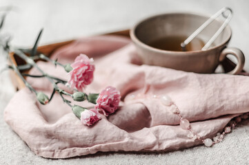 A wooden tray with a linen napkin, brewed herbal tea, pink carnations and rose quartz beads on a woolen blanket closeup.