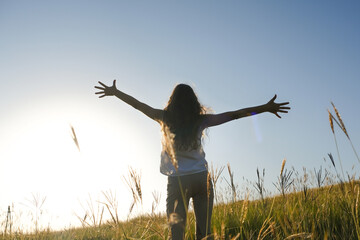 A young girl with long, wavy hair stood with her back outstretched against the blue sky.