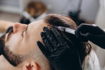 An attractive man receives mesotherapy injections to treat hair loss at the clinic. Injections into...