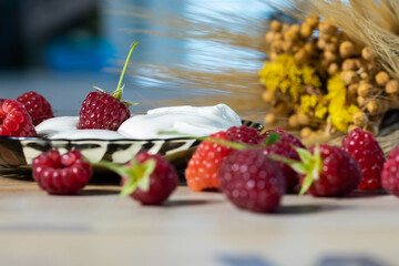 Delicious dessert of raspberries and sour cream on the table among the scattered raspberries.