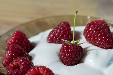 Ripe raspberry berry with a sprig in sour cream on the table.